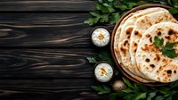 Fresh homemade naan bread served with yogurt dip and herbs on rustic wooden background, traditional Indian flatbread with charred spots and soft texture.