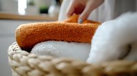 Clean folded towels in woven basket, orange and white cotton terry cloth textiles stacked neatly for bathroom or spa setting, soft focus composition.