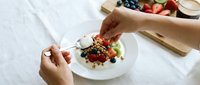 Chef hands plating gourmet dessert with fresh berries and chocolate sauce on white plate in professional kitchen setting for fine dining presentation.