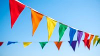 Colorful bunting flags strung across clear blue sky, featuring red, orange, yellow, green, blue and purple triangular pennants for festive celebrations, parties and outdoor events.