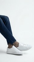 Casual white sneakers and blue jeans on neutral background for fashion and lifestyle concepts.