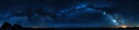 Panoramic view of Milky Way galaxy arching across dark night sky with silhouetted landscape and glowing stars creating dramatic celestial scenery.