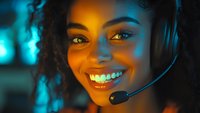Smiling African American female customer service representative wearing headset with microphone in modern office with colorful lighting for business communications.