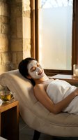 Young Asian woman relaxing with clay face mask at luxury spa, wrapped in towel, warm candlelight ambiance, green tea nearby.