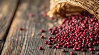 Red adzuki beans spilling from woven basket onto rustic wooden table surface, natural lighting creates warm atmosphere for food photography and culinary design.