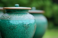 Decorative turquoise ceramic pot with ornate spiral patterns and wooden lid against blurred green garden background, showcasing traditional Asian pottery craftsmanship.