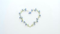 Heart-shaped frame made of delicate blue forget-me-not flowers and green stems on white background for romantic designs and spring decorations.