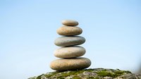 Zen stone stack balanced on moss-covered rock against clear blue sky background for meditation wellness and mindfulness concepts.