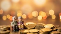 Elderly couple figurines sitting on golden coins with bokeh background, symbolizing retirement savings and financial security for seniors.