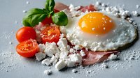 Sunny side up egg with crispy bacon, crumbled feta cheese, fresh cherry tomatoes and basil leaves on gray background, sprinkled with sea salt flakes.