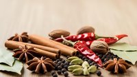 Aromatic spices including cinnamon sticks, star anise, cardamom pods, peppercorns and chili peppers arranged on wooden surface for cooking.