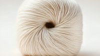 Soft cream-colored yarn ball with spiral texture and natural fiber details on white background, showing delicate twisted strands in macro photography.