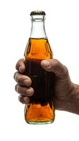 Hand holding glass bottle filled with cola beverage against white background. Isolated stock photo suitable for advertising, packaging design, and beverage marketing campaigns.