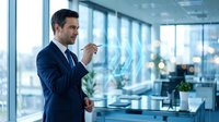 Professional businessman in navy suit presenting data analytics on transparent digital screen in modern office with city view windows.