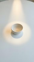 Empty white ceramic bowl on clean white surface with dramatic overhead lighting creating soft shadows for minimalist kitchen design concepts.
