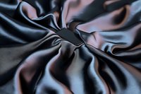 Luxurious black silk fabric with elegant folds and creases creating dramatic light and shadow effects, smooth flowing textile surface with subtle sheen and reflections.