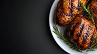 Grilled chicken thighs with crispy charred skin and fresh rosemary sprigs served on white plate against dark background. Dramatic food photography.
