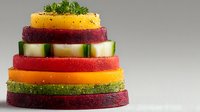 Colorful layered vegetable tower with cucumber, carrot, beetroot and herbs stacked in pyramid formation on white background for healthy eating concepts.