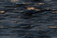Dark textured stone surface with golden highlights creating dramatic natural pattern. Rough layered rock formation with metallic copper accents in moody lighting.