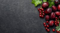 Fresh red currants and dried cranberries with green parsley leaves arranged on dark stone background with copy space for text, food photography.