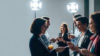 Diverse business professionals networking at corporate event with drinks and casual conversation in modern office setting.