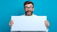 Excited bearded man with glasses holding blank white poster against vibrant blue background, perfect for adding custom text or promotional message.