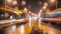 Dynamic urban street scene with colorful light trails from moving traffic on wet asphalt at night, creating motion blur effect with bokeh lights in background.