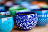 Colorful ceramic bowls with traditional dotted patterns and geometric designs in blue, turquoise and green tones arranged on wooden surface. Artisanal pottery.