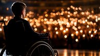 Person in wheelchair silhouetted against glowing city lights at night, creating atmospheric mood of contemplation and hope. View from behind captures peaceful solitude.