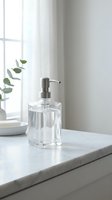 Clear glass soap dispenser on white marble countertop in bright minimalist bathroom with eucalyptus branch and natural window light for home decor.