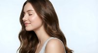 Young woman with long wavy brown hair and closed eyes showing peaceful expression against white background for beauty and wellness concepts.