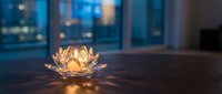 Crystal lotus flower candle holder glowing warmly on wooden table in modern apartment with city lights bokeh background creating peaceful ambiance.