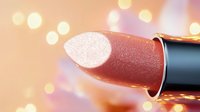 Luxurious metallic rose gold lipstick closeup with soft bokeh lights background, makeup product photography for cosmetic advertising and beauty industry.