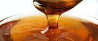 Honey dripping from wooden dipper into bowl, golden liquid flowing, natural sweetener for cooking and baking projects.