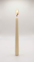 Lit ivory taper candle with glowing flame isolated on white background, evoking warmth, elegance, and ambiance for holiday and home decor.