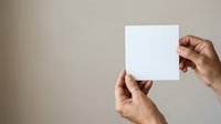 Adult male with medium brown skin tone holding blank white square card or paper against neutral beige background, suitable for mockups, presentations, and advertising campaigns.