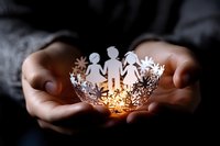 Hands holding delicate paper cutout of family figures in illuminated decorative bowl, symbolizing care, protection, and family unity.