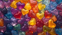 Colorful heart-shaped gummy candies in assorted vibrant colors including red, yellow, purple, blue and orange arranged closely together as a full frame background for confectionery and sweet treat designs.
