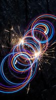 Colorful light trails and golden sparks create dynamic swirling patterns against dark textured surface for creative design projects.