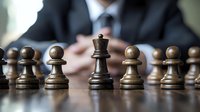 Business professional in suit with chess pieces on table, queen standing among pawns symbolizing leadership strategy and corporate hierarchy in competitive environment.