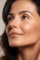 Close-up portrait of young Hispanic woman with glowing natural makeup and flawless skin looking up with gentle smile against neutral background.
