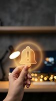 Hand holding glowing bell icon with exclamation mark against blurred office background, representing notification, alert, and communication for business and technology concepts.
