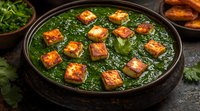 Palak paneer curry with golden fried cottage cheese cubes in rich green spinach gravy, served in rustic clay bowl on dark background. Traditional Indian food.