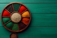 Colorful spices and seasonings arranged in wooden compartmented circular tray on green wooden background, overhead view of traditional cooking ingredients.