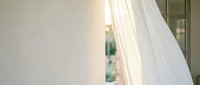 Sheer white curtain billowing gently near an open window with natural sunlight streaming through, creating soft shadows and an airy, serene atmosphere for home decor and interior design projects.