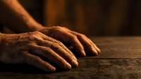 Elderly hands resting on wooden table surface showing age and wisdom in warm golden lighting for healthcare and aging concepts.