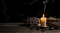 Mystical altar setup with burning candle, pentagram, dried herbs and ritual tools on dark wooden surface with atmospheric smoke for spiritual practices.