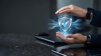 Businessman hands protecting digital security shield with checkmark hologram above computer keyboard for cybersecurity and data protection concepts.