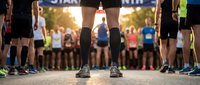 Runner in black compression socks and athletic shoes stands at starting line with diverse group of marathon participants gathered behind during sunrise community race event.