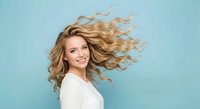 Young blonde woman with flowing wavy hair in motion against blue background, expressing joy and freedom for beauty and lifestyle concepts.